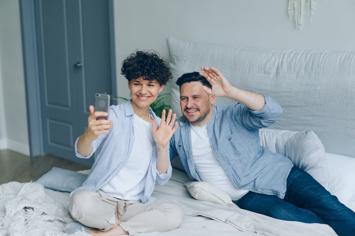 Two people sitting together at home, waving at a phone screen