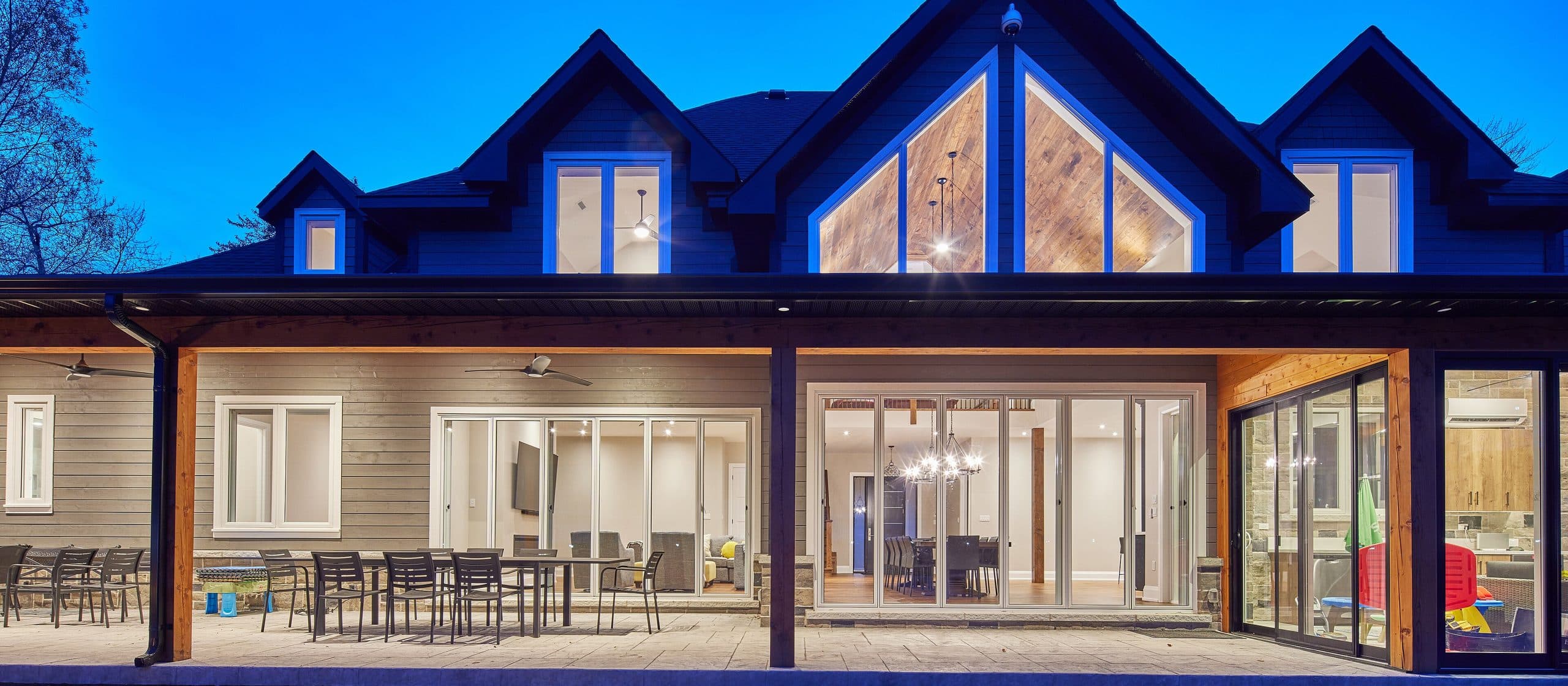 A modern two-storey house at dusk, lights on inside and the patio doors open